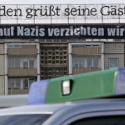 Polizeifahrzeuge stehen vor einem Hochhaus, an dem unter der Leuchreklame Dresden grüßt seine Gäste ein Zusatztransparent mit dem Schriftzug Auf Nazis verzichten wir! aufgehangen wurde.